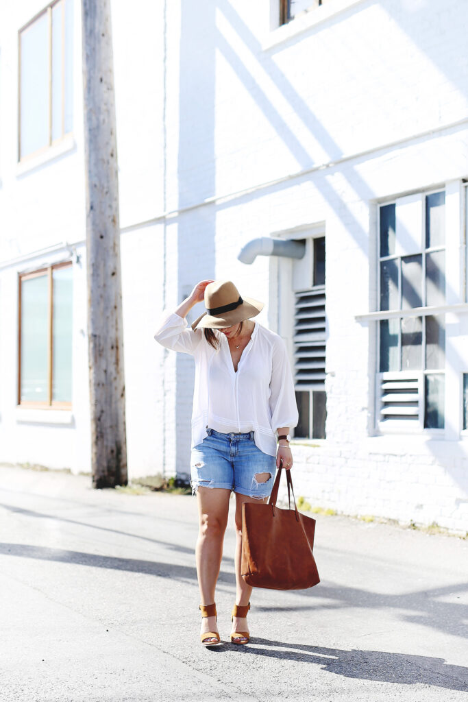 Denim cut-offs, white blouse, floppy hat, leather tote.