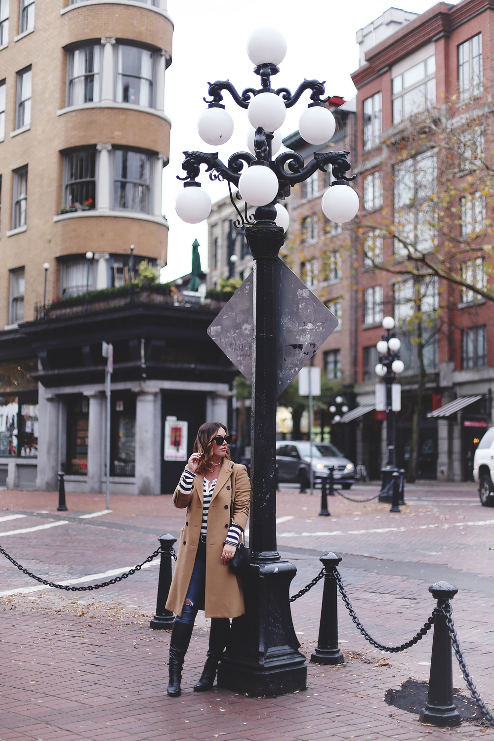 To Vogue or Bust shares camel coat outfit ideas in a camel Aritzia wilfred coat, Mavi skinny jeans, striped Gentle Fawn top, La Canadienne boots and Celine sunglasses in Gastown, Vancouver