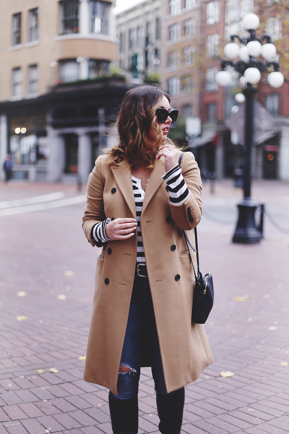 To Vogue or Bust shares camel coat outfit ideas in a camel Aritzia wilfred coat, Mavi skinny jeans, striped Gentle Fawn top, La Canadienne boots and Celine sunglasses in Gastown, Vancouver