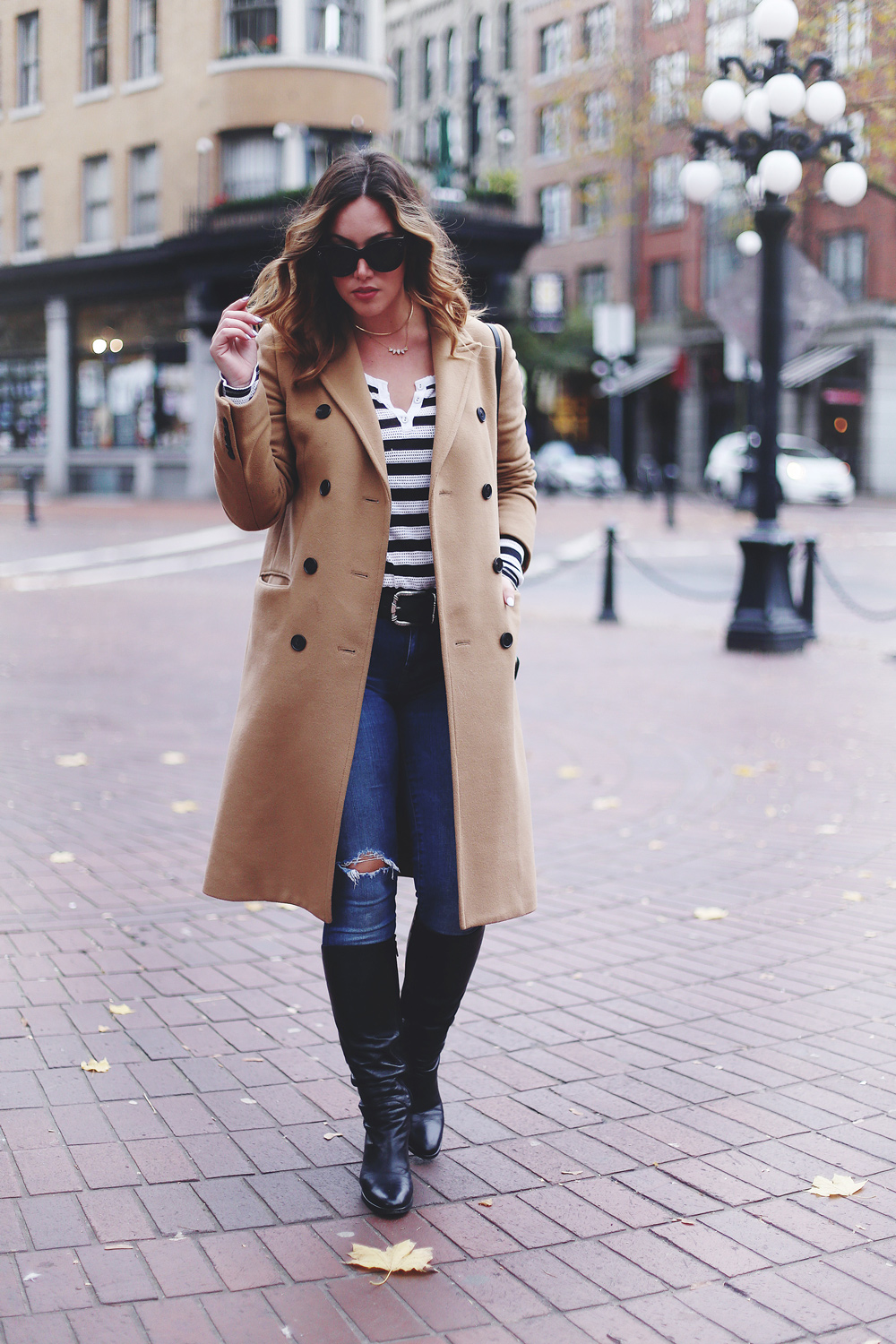 To Vogue or Bust shares camel coat outfit ideas in a camel Aritzia wilfred coat, Mavi skinny jeans, striped Gentle Fawn top, La Canadienne boots and Celine sunglasses in Gastown, Vancouver