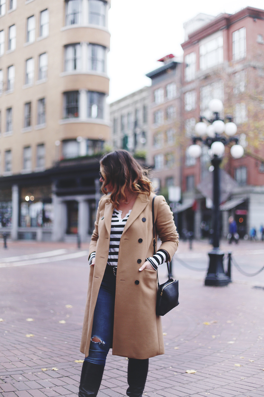 To Vogue or Bust shares camel coat outfit ideas in a camel Aritzia wilfred coat, Mavi skinny jeans, striped Gentle Fawn top, La Canadienne boots and Celine sunglasses in Gastown, Vancouver