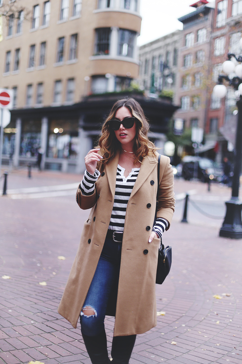 To Vogue or Bust shares camel coat outfit ideas in a camel Aritzia wilfred coat, Mavi skinny jeans, striped Gentle Fawn top, La Canadienne boots and Celine sunglasses in Gastown, Vancouver